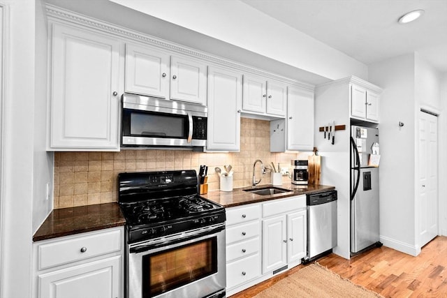 kitchen featuring white cabinets, a sink, light wood finished floors, appliances with stainless steel finishes, and backsplash