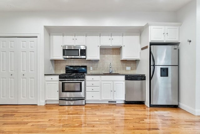 kitchen featuring light wood-type flooring, white cabinets, tasteful backsplash, a sink, and appliances with stainless steel finishes