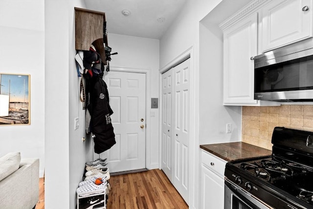 kitchen featuring appliances with stainless steel finishes, light wood finished floors, dark stone counters, white cabinetry, and backsplash