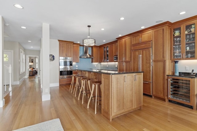 30 Preston Ct Unit 1, Swampscott, MA 01907 - kitchen featuring beverage cooler, stainless steel appliances, wall chimney range hood, brown cabinets, and light wood-type flooring