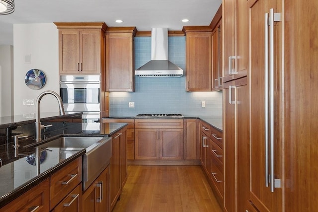 30 Preston Ct Unit 1, Swampscott, MA 01907 - kitchen featuring wall chimney range hood, light wood finished floors, brown cabinets, dark stone countertops, and recessed lighting