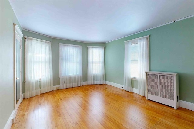 spare room featuring ornamental molding, radiator heating unit, and light wood-type flooring