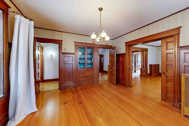 unfurnished dining area with crown molding, an inviting chandelier, and light hardwood / wood-style floors