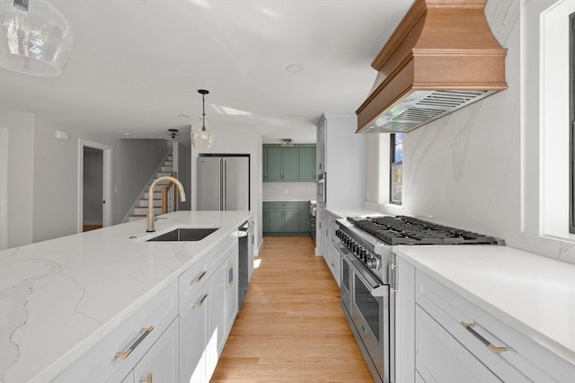 kitchen with white cabinets, premium range hood, sink, hanging light fixtures, and high quality appliances