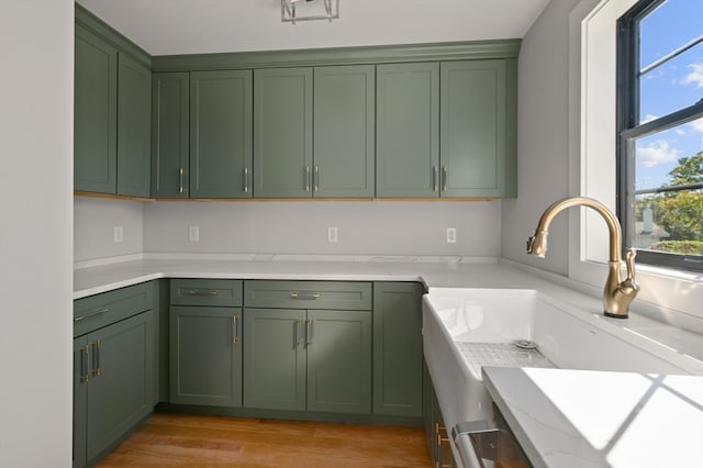 kitchen with light stone counters, green cabinetry, light wood-type flooring, and sink