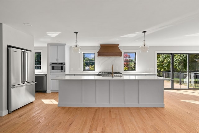 kitchen featuring hanging light fixtures, stainless steel appliances, light wood-type flooring, and custom range hood