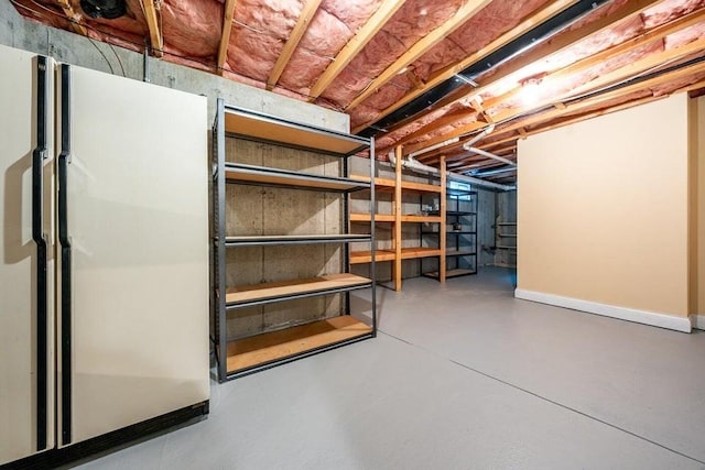 unfinished basement featuring baseboards and freestanding refrigerator