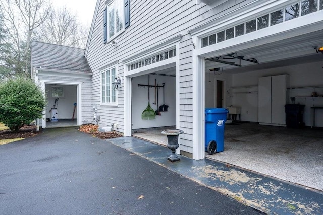 exterior space with aphalt driveway, a garage, roof with shingles, and a sink