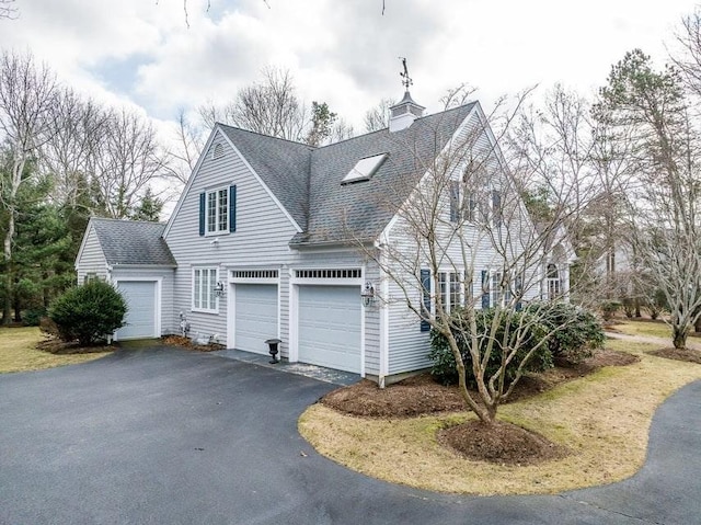 view of side of home featuring aphalt driveway, an attached garage, roof with shingles, and a chimney