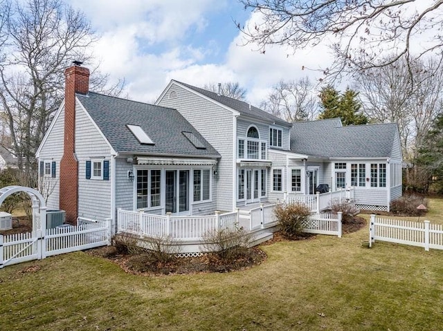 back of property with fence, roof with shingles, a chimney, a deck, and a yard