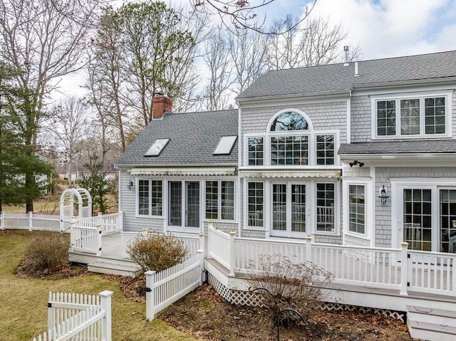 rear view of property with a chimney, roof with shingles, a deck, and fence