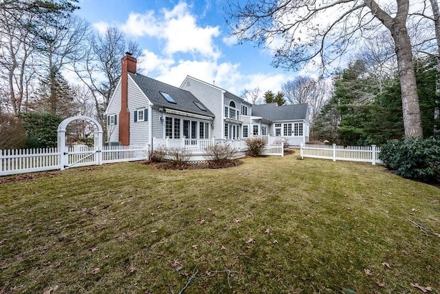 back of property with a lawn, a deck, a gate, a fenced backyard, and a chimney