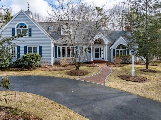 view of front of home featuring driveway, a chimney, and roof with shingles