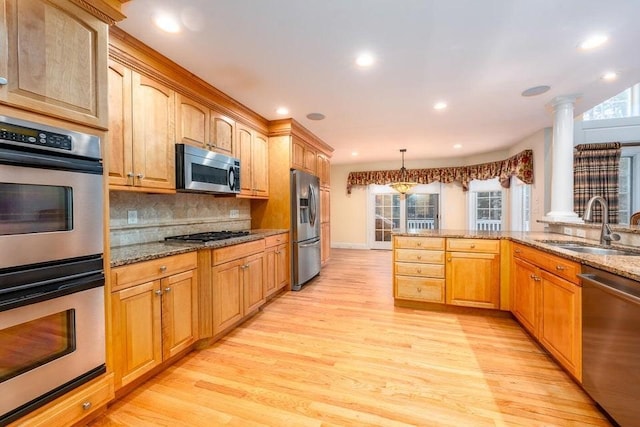 kitchen with light wood-style flooring, a sink, light stone counters, appliances with stainless steel finishes, and decorative backsplash