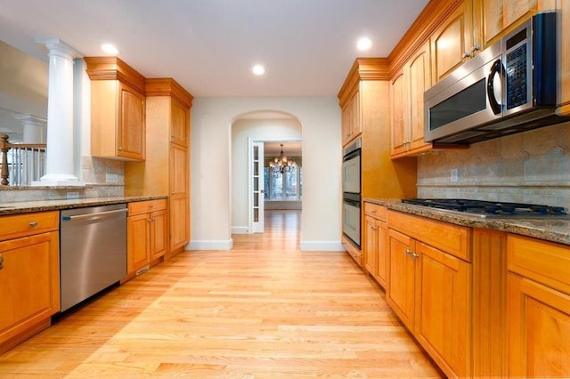 kitchen featuring light wood-style flooring, stainless steel appliances, arched walkways, an inviting chandelier, and stone counters