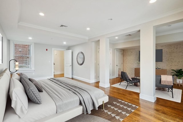 bedroom featuring ensuite bathroom, light hardwood / wood-style flooring, ornamental molding, and brick wall