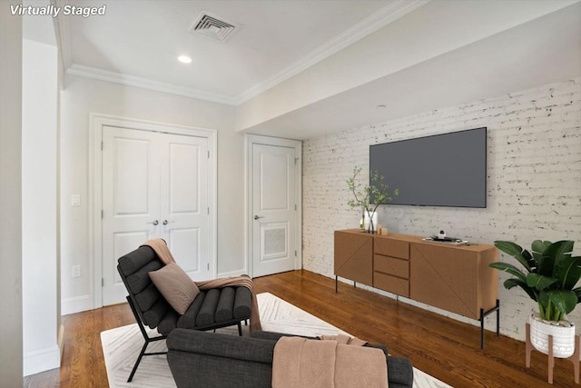 living room with crown molding, wood-type flooring, and brick wall