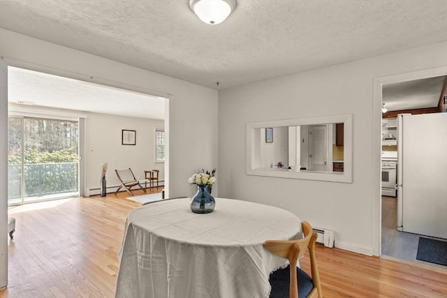 dining area featuring light wood-style floors, a baseboard heating unit, baseboard heating, and a textured ceiling