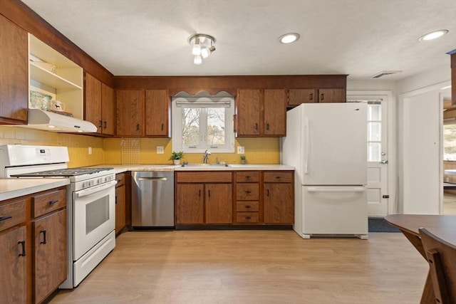 kitchen with light wood-type flooring, under cabinet range hood, a sink, white appliances, and light countertops