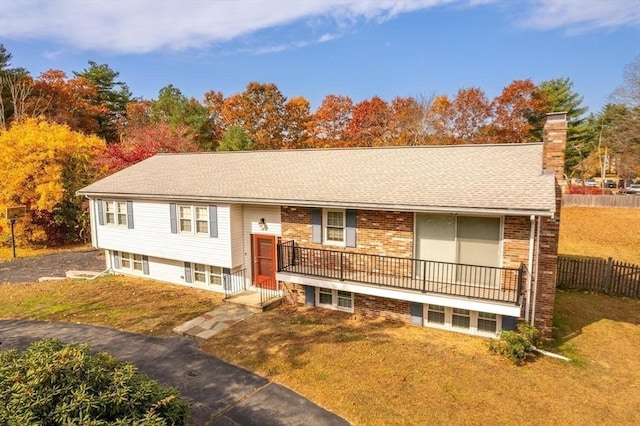 raised ranch with a front lawn, fence, a shingled roof, brick siding, and a chimney