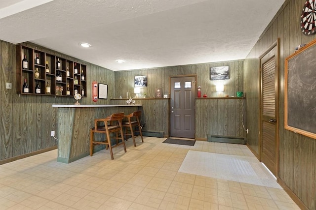 bar with baseboard heating, wood walls, a bar, and baseboards