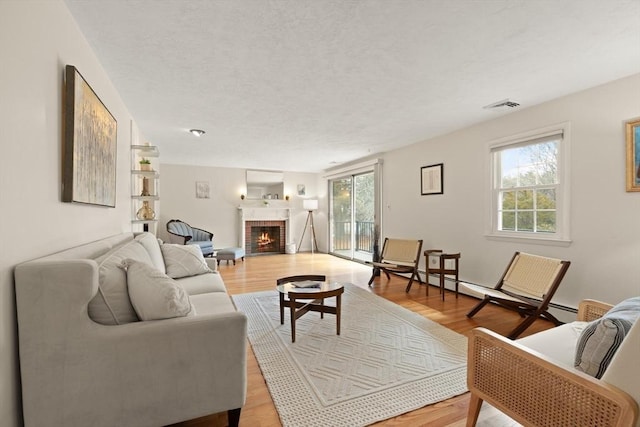 living room with light wood finished floors, visible vents, a brick fireplace, and a textured ceiling