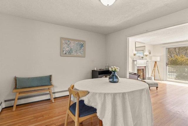 dining area with a baseboard radiator, a fireplace, a textured ceiling, and wood finished floors