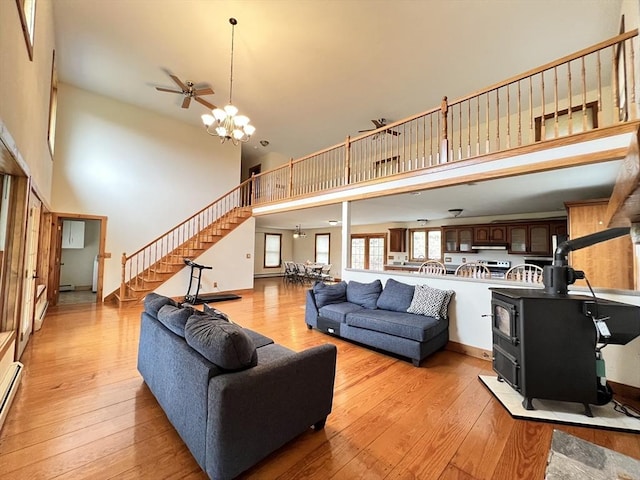 living room with light wood-style flooring, ceiling fan with notable chandelier, a high ceiling, and stairway