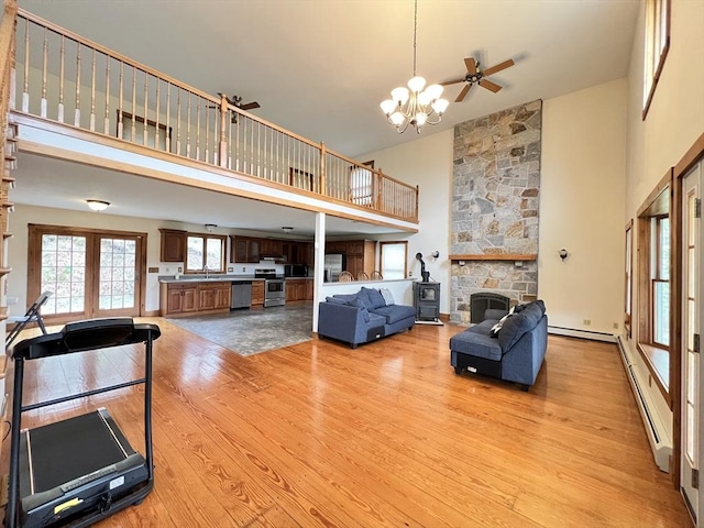 living area featuring high vaulted ceiling, a baseboard heating unit, light wood-type flooring, and a stone fireplace