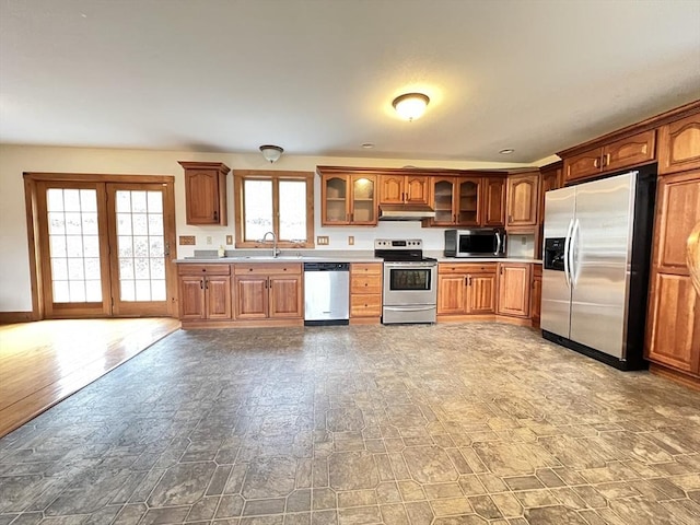 kitchen featuring glass insert cabinets, light countertops, under cabinet range hood, a sink, and appliances with stainless steel finishes