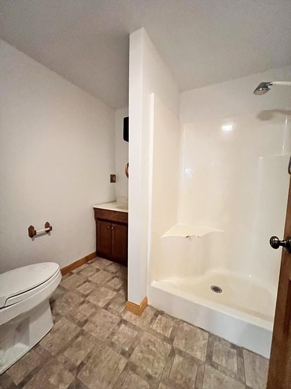 bathroom featuring toilet, baseboards, walk in shower, and vanity