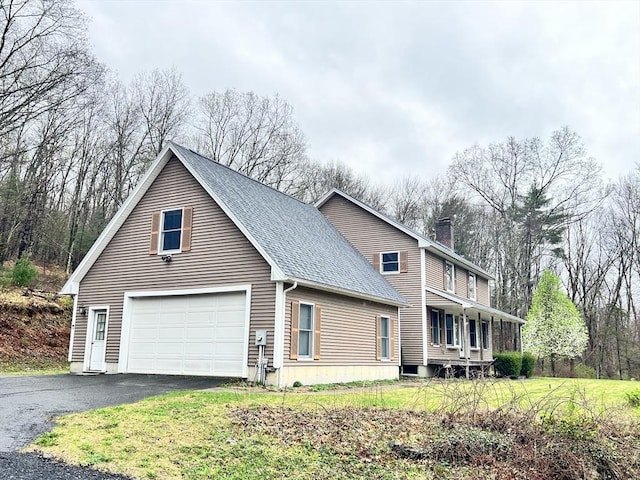 view of home's exterior featuring roof with shingles, a detached garage, a chimney, a lawn, and driveway