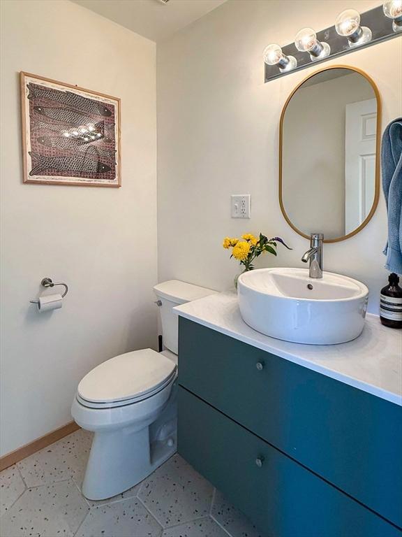 half bathroom featuring toilet, baseboards, and vanity