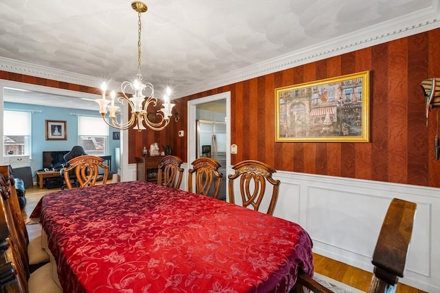 dining room with crown molding, wainscoting, a notable chandelier, and wood finished floors