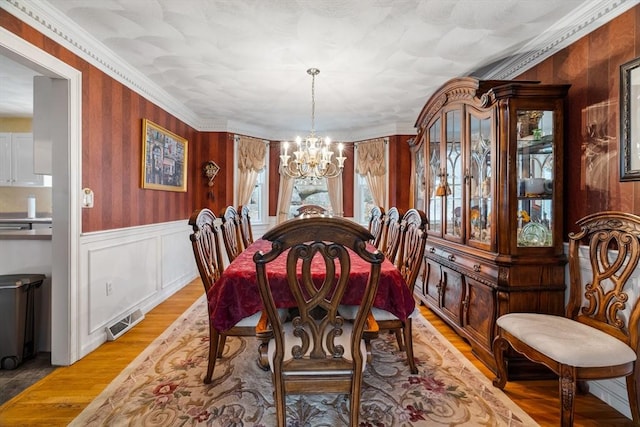 dining room with visible vents, a wainscoted wall, crown molding, light wood-type flooring, and a notable chandelier