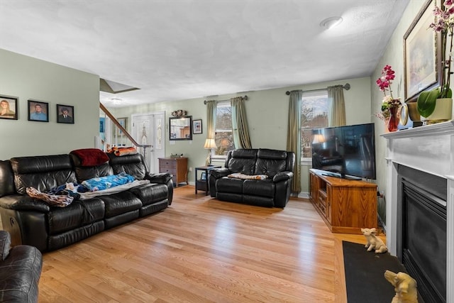 living area featuring light wood-type flooring, stairway, and a glass covered fireplace