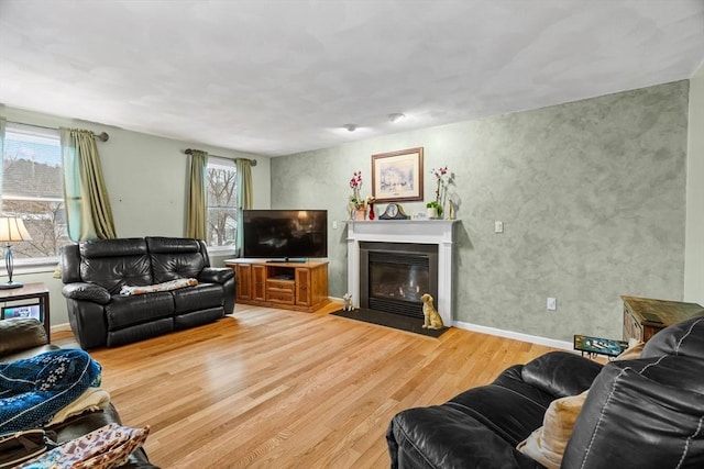 living area featuring a fireplace with flush hearth, light wood-style flooring, and baseboards