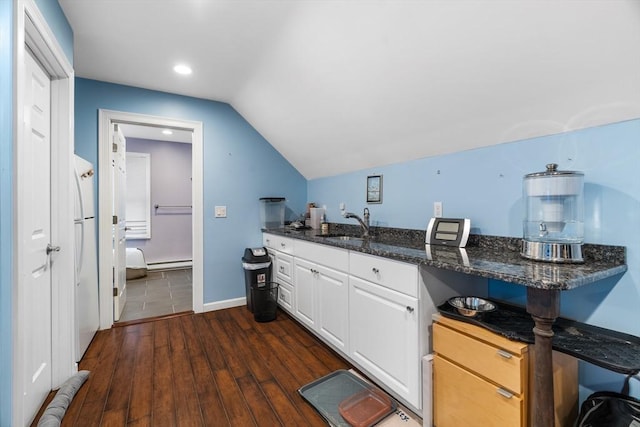 kitchen featuring dark wood-type flooring, white cabinetry, vaulted ceiling, a sink, and dark stone countertops