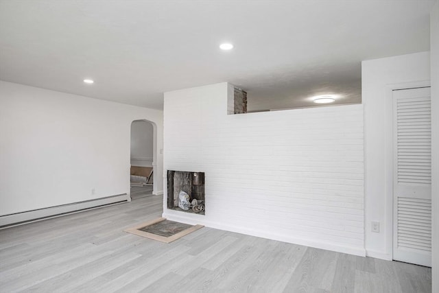 unfurnished living room featuring a multi sided fireplace, a baseboard heating unit, and light wood-type flooring