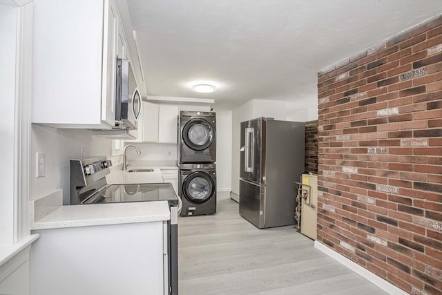 kitchen with stacked washer / drying machine, light hardwood / wood-style floors, white cabinetry, stainless steel appliances, and brick wall