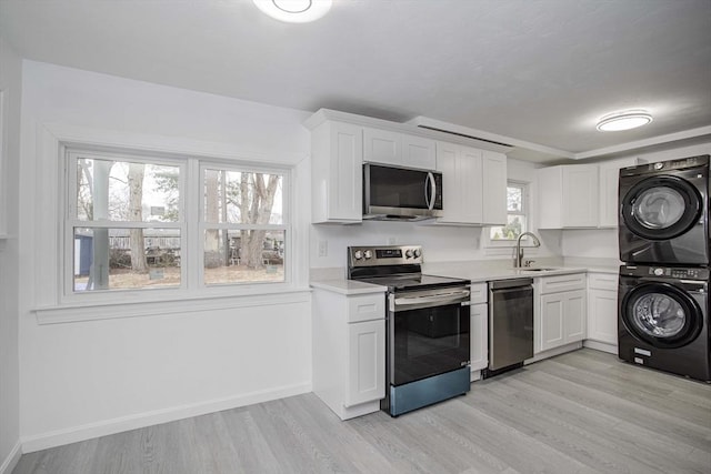 kitchen with light wood-type flooring, stainless steel appliances, sink, stacked washer and clothes dryer, and white cabinetry