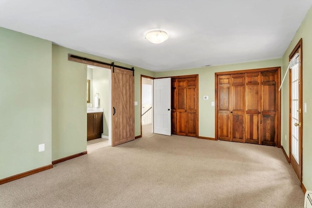 unfurnished bedroom featuring two closets, ensuite bath, light colored carpet, and a barn door