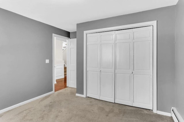 unfurnished bedroom with a baseboard heating unit, light carpet, and a closet