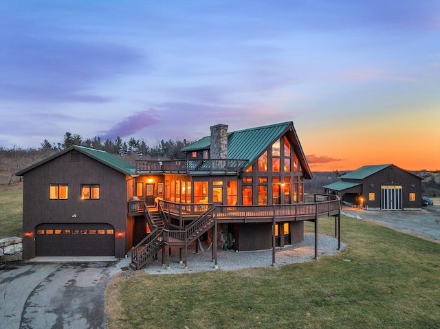 back house at dusk featuring a yard, a deck, and a garage