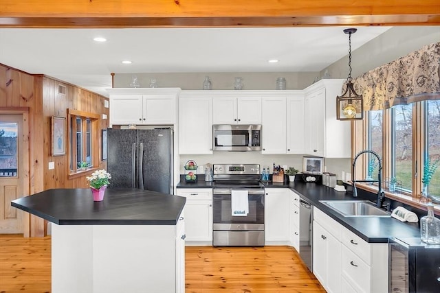 kitchen featuring sink, stainless steel appliances, wood walls, decorative light fixtures, and white cabinets