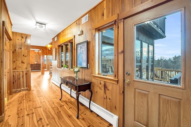 doorway with light hardwood / wood-style flooring, wooden walls, and a baseboard heating unit