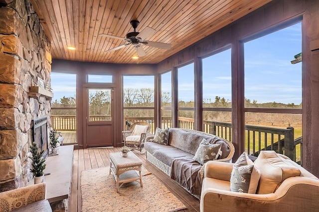 sunroom / solarium featuring a stone fireplace, a healthy amount of sunlight, ceiling fan, and wooden ceiling