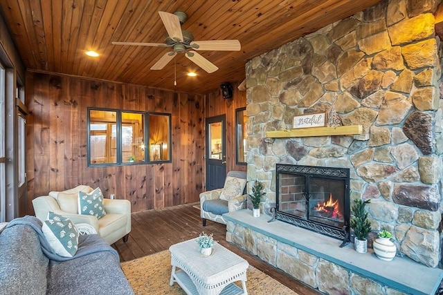 unfurnished living room featuring wooden ceiling, a stone fireplace, wooden walls, ceiling fan, and wood-type flooring