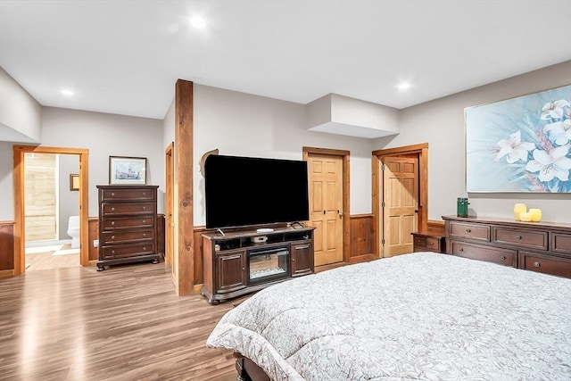 bedroom featuring ensuite bathroom, light wood-type flooring, and wooden walls