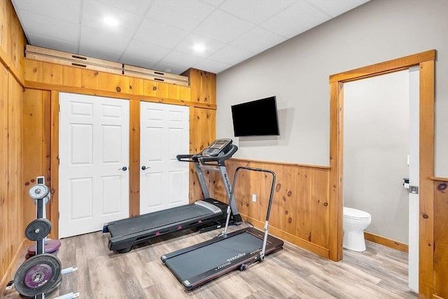 workout area with a paneled ceiling, wood walls, and light hardwood / wood-style flooring